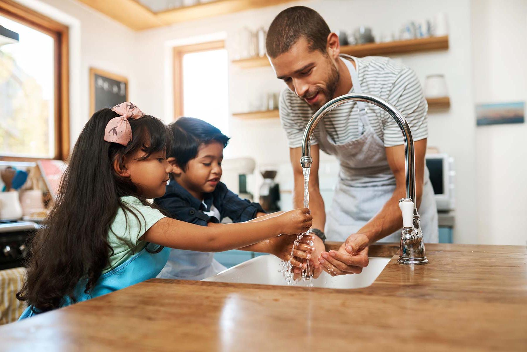 A man and two children wash hands at a kitchen sink